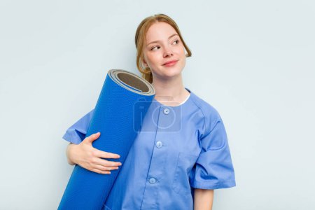 Photo for Young caucasian physiotherapist holding a mat isolated on blue background dreaming of achieving goals and purposes - Royalty Free Image