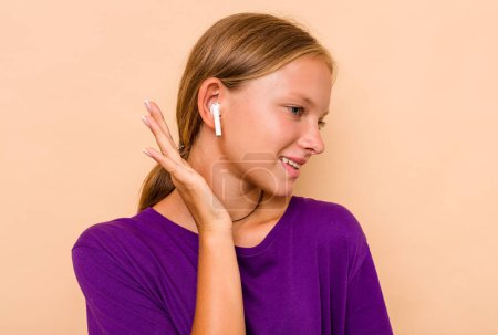 Foto de Pequeña chica caucásica escuchando música aislada sobre fondo beige - Imagen libre de derechos