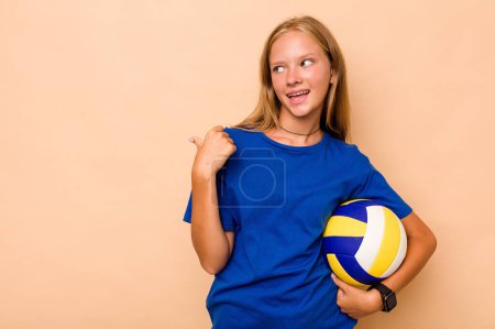 Photo for Little caucasian girl playing volleyball isolated on beige background points with thumb finger away, laughing and carefree. - Royalty Free Image