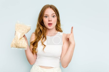 Téléchargez les photos : Jeune femme caucasienne tenant la farine d'avoine isolée sur fond bleu pointant vers le côté - en image libre de droit