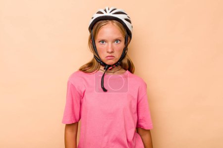 Photo for Little caucasian girl wearing a bike helmet isolated on beige background shrugs shoulders and open eyes confused. - Royalty Free Image