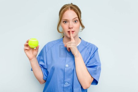 Foto de Joven fisioterapeuta caucásica sosteniendo una pelota de tenis aislada sobre fondo azul manteniendo un secreto o pidiendo silencio. - Imagen libre de derechos