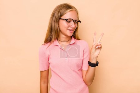 Foto de Caucásico adolescente chica aislado en beige fondo alegre y despreocupado mostrando un símbolo de paz con los dedos. - Imagen libre de derechos