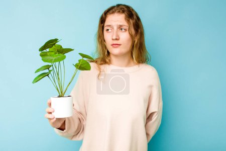 Photo for Young caucasian woman holding a plant isolated on blue background confused, feels doubtful and unsure. - Royalty Free Image