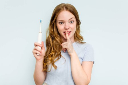 Foto de Mujer caucásica joven sosteniendo cepillo de dientes eléctrico aislado sobre fondo azul manteniendo un secreto o pidiendo silencio. - Imagen libre de derechos