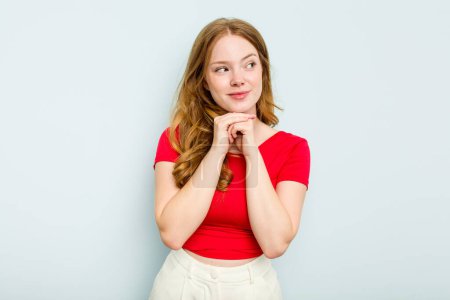 Photo for Young caucasian woman isolated on blue background keeps hands under chin, is looking happily aside. - Royalty Free Image