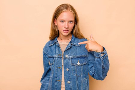 Foto de Caucásico adolescente chica aislado en beige fondo persona apuntando a mano a una camisa copia espacio, orgulloso y seguro de sí mismo - Imagen libre de derechos
