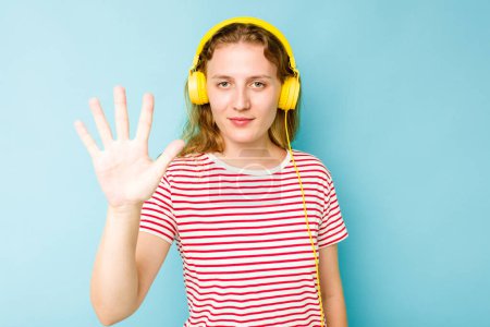 Téléchargez les photos : Jeune femme caucasienne portant des écouteurs isolés sur fond bleu souriant gai montrant numéro cinq avec les doigts. - en image libre de droit
