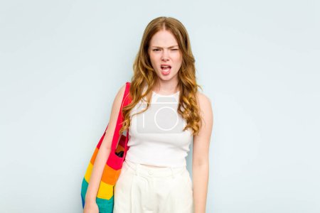 Foto de Joven mujer caucásica sosteniendo LGTBI bolsa aislada sobre fondo azul gritando muy enojado y agresivo. - Imagen libre de derechos