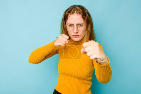 Photo for Young caucasian woman isolated on blue background throwing a punch, anger, fighting due to an argument, boxing. - Royalty Free Image