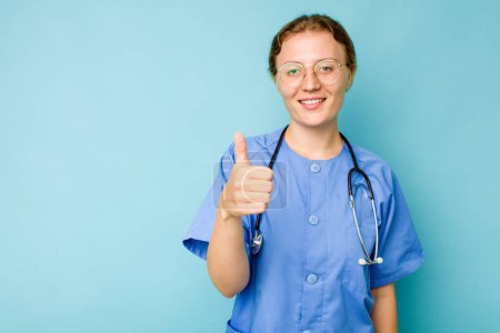 Photo for Young nurse caucasian woman isolated on blue background smiling and raising thumb up - Royalty Free Image