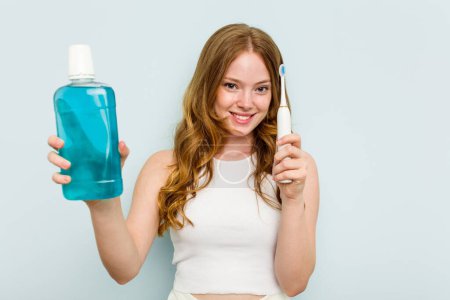 Téléchargez les photos : Jeune femme caucasienne tenant un rince-bouche et une brosse à dents isolés sur fond bleu - en image libre de droit