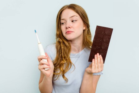 Téléchargez les photos : Jeune femme caucasienne tenant chocolat et brosse à dents isolés sur fond bleu - en image libre de droit