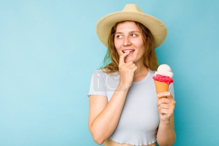 Téléchargez les photos : Jeune femme caucasienne tenant une crème glacée isolé un fond bleu détendu penser à quelque chose en regardant un espace de copie. - en image libre de droit