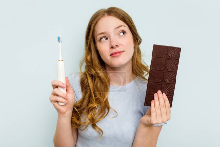 Photo for Young caucasian woman holding chocolate and toothbrush isolated on blue background - Royalty Free Image