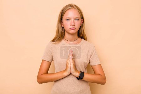 Photo for Caucasian teen girl isolated on beige background praying, showing devotion, religious person looking for divine inspiration. - Royalty Free Image