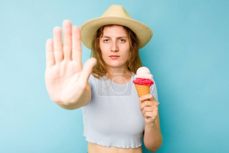 Téléchargez les photos : Jeune femme caucasienne tenant une crème glacée isolé un fond bleu debout avec la main tendue montrant stop signe, vous empêchant. - en image libre de droit