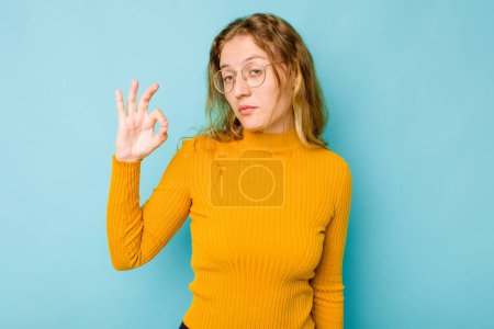 Photo for Young caucasian woman isolated on blue background winks an eye and holds an okay gesture with hand. - Royalty Free Image