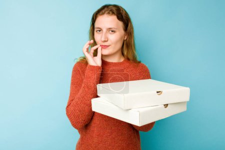 Téléchargez les photos : Jeune femme caucasienne tenant des boîtes de pizzas isolées sur fond bleu avec les doigts sur les lèvres gardant un secret. - en image libre de droit