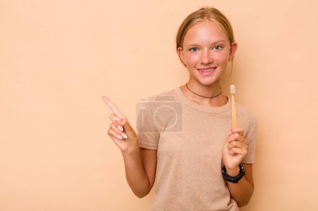 Foto de Caucásico adolescente chica cepillado dientes aislado en beige fondo sonriendo y señalando a un lado, mostrando algo en espacio en blanco. - Imagen libre de derechos
