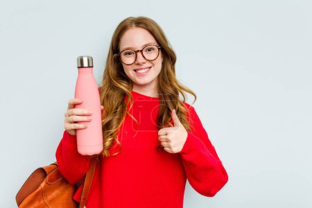 Photo for Young student woman holding a canteen isolated on blue background smiling and raising thumb up - Royalty Free Image