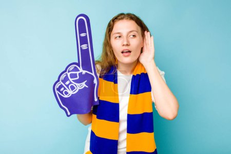 Téléchargez les photos : Jeune femme caucasienne fan de sport isolé sur fond bleu en essayant d'écouter un potins. - en image libre de droit