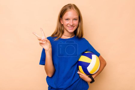 Téléchargez les photos : Petite fille caucasienne jouant au volley isolé sur fond beige joyeux et insouciant montrant un symbole de paix avec les doigts. - en image libre de droit