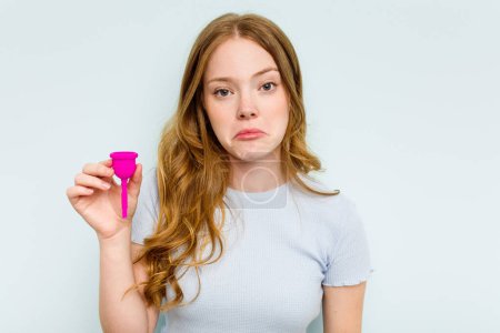 Photo for Young caucasian woman holding menstrual cup isolated on blue background shrugs shoulders and open eyes confused. - Royalty Free Image