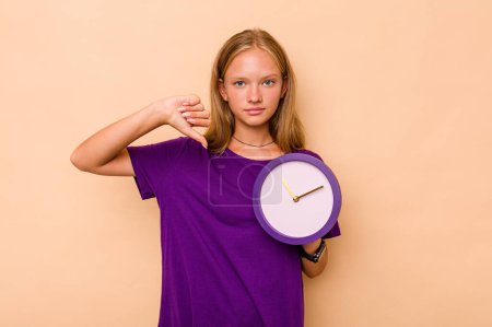 Photo for Little caucasian girl holding a clock isolated on beige background showing a dislike gesture, thumbs down. Disagreement concept. - Royalty Free Image