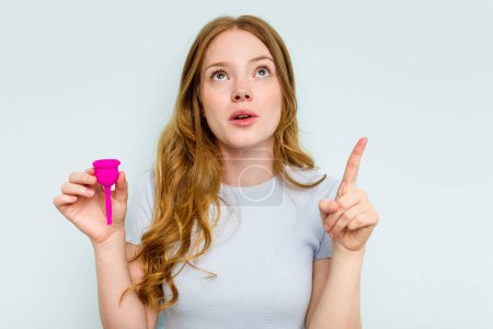 Téléchargez les photos : Jeune femme caucasienne tenant la coupe menstruelle isolée sur fond bleu pointant à l'envers avec bouche ouverte. - en image libre de droit