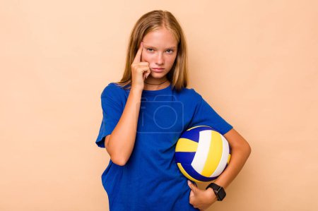 Téléchargez les photos : Petite fille caucasienne jouant au volley isolé sur fond beige pointant temple avec le doigt, pensant, concentré sur une tâche. - en image libre de droit