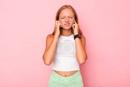 Téléchargez les photos : Blanc adolescent fille isolé sur fond rose couvrant les oreilles avec les doigts, stressé et désespéré par un ambiant bruyant. - en image libre de droit