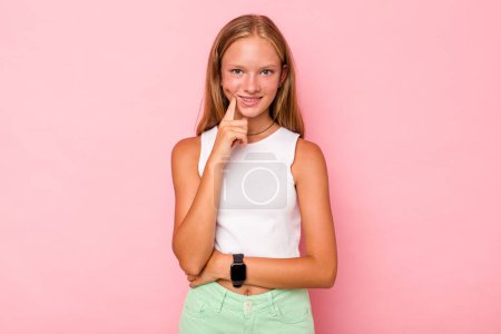 Foto de Caucásico adolescente chica aislado en rosa fondo sonriendo feliz y seguro de sí mismo, tocando la barbilla con la mano. - Imagen libre de derechos
