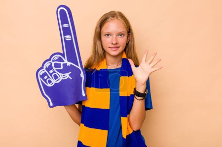 Foto de Poco caucásico deportes fan chica aislado en beige fondo sonriendo alegre mostrando número cinco con los dedos. - Imagen libre de derechos