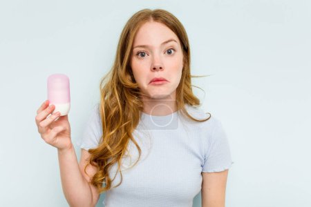 Photo for Young caucasian woman holding deodorant isolated on blue background shrugs shoulders and open eyes confused. - Royalty Free Image