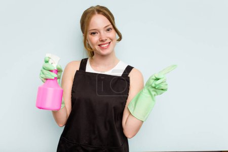 Photo for Young cleaner woman isolated on blue background smiling and pointing aside, showing something at blank space. - Royalty Free Image