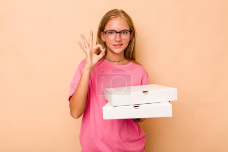 Téléchargez les photos : Petite fille caucasienne tenant pizza isolé sur fond beige joyeux et confiant montrant ok geste. - en image libre de droit
