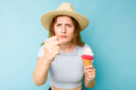 Téléchargez les photos : Jeune femme caucasienne tenant une crème glacée isolé un fond bleu montrant poing à caméra, expression faciale agressive. - en image libre de droit