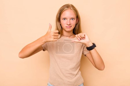Foto de Caucásico adolescente chica aislado en beige fondo mostrando pulgares hacia arriba y pulgares hacia abajo, difícil elegir concepto - Imagen libre de derechos