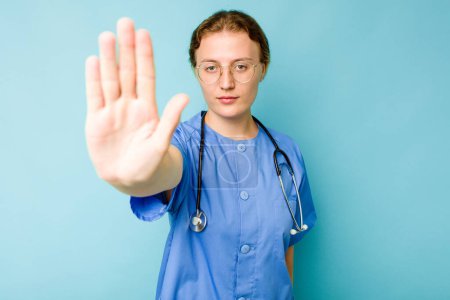 Téléchargez les photos : Jeune infirmière caucasienne isolée sur fond bleu debout avec la main tendue montrant le signe d'arrêt, vous empêchant. - en image libre de droit