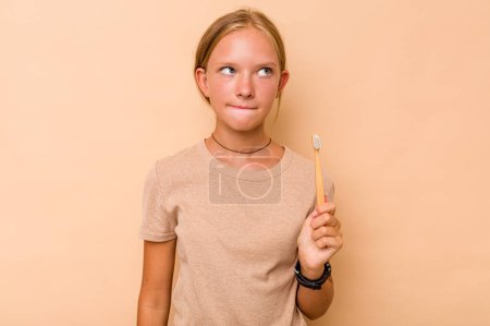 Foto de Caucásico adolescente chica cepillarse los dientes aislado en beige fondo confundido, se siente dudoso e inseguro. - Imagen libre de derechos