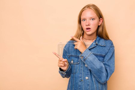 Téléchargez les photos : Caucasienne adolescent fille isolé sur fond beige pointant avec les index vers un espace de copie, exprimant l'excitation et le désir. - en image libre de droit