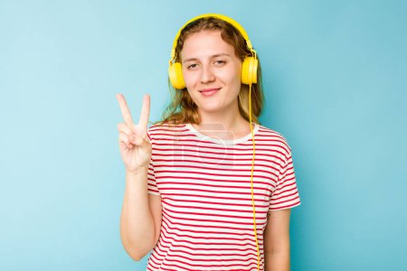 Téléchargez les photos : Jeune femme caucasienne portant des écouteurs isolés sur fond bleu montrant le numéro deux avec les doigts. - en image libre de droit