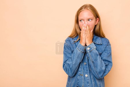 Foto de Caucásico adolescente chica aislado en beige fondo reflexivo mirando a un espacio de copia que cubre la boca con la mano. - Imagen libre de derechos