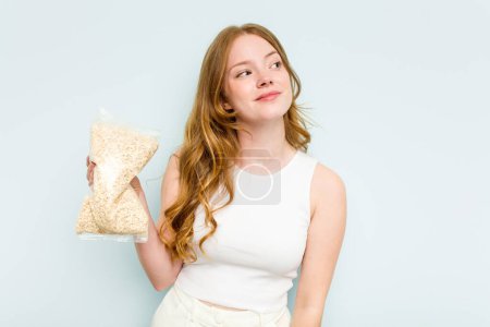 Photo for Young caucasian woman holding oatmeal isolated on blue background dreaming of achieving goals and purposes - Royalty Free Image