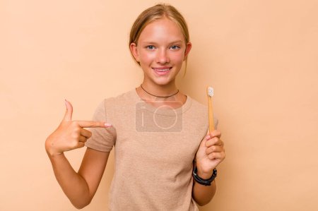Foto de Caucásico adolescente chica cepillarse los dientes aislado en beige fondo persona señalando a mano a un espacio de copia de la camisa, orgulloso y seguro - Imagen libre de derechos