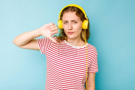 Téléchargez les photos : Jeune femme caucasienne portant des écouteurs isolés sur fond bleu montrant un geste détestable, pouces baissés. Concept de désaccord. - en image libre de droit