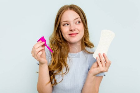 Téléchargez les photos : Jeune caucasien tenant coupe menstruelle et serviette hygiénique isolé sur fond bleu - en image libre de droit