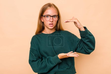 Foto de Caucásico adolescente chica aislado en beige fondo sosteniendo algo con ambas manos, presentación del producto. - Imagen libre de derechos