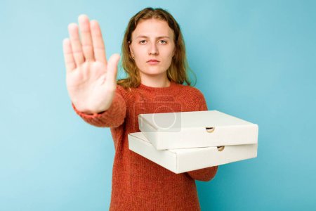 Téléchargez les photos : Jeune femme caucasienne tenant des boîtes de pizzas isolées sur fond bleu debout avec la main tendue montrant le panneau stop, vous empêchant. - en image libre de droit